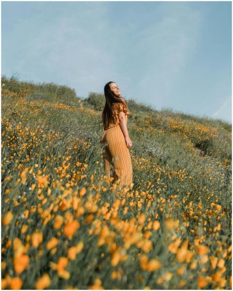 A woman in a yellow dress smiles amidst lush poppy
