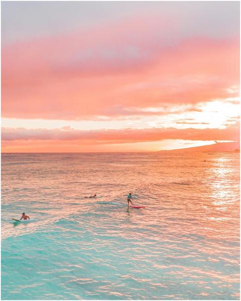 Surfers riding the waves during a stunning pink su