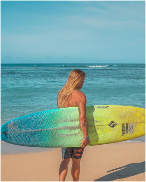 A surfer with tattoos holding a vibrant surfboard