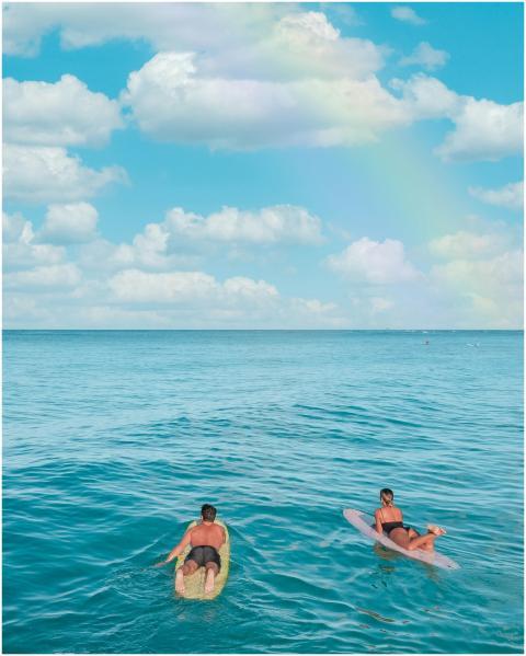 Two surfers paddling out on a calm ocean under a b