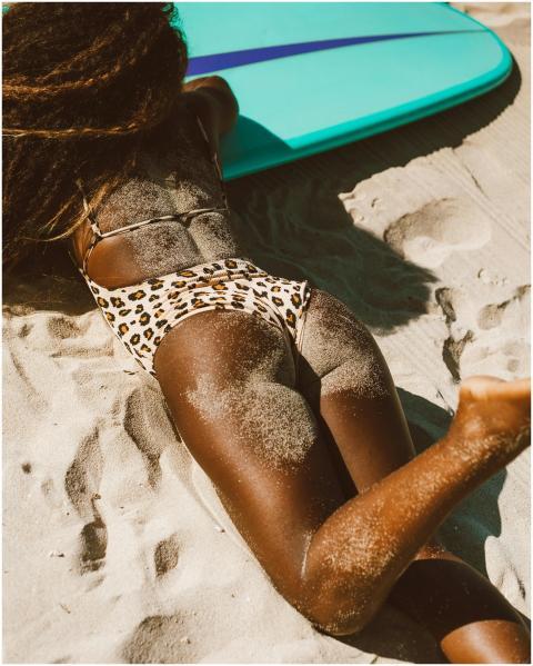 A woman with curly hair lies on a sandy beach, sun