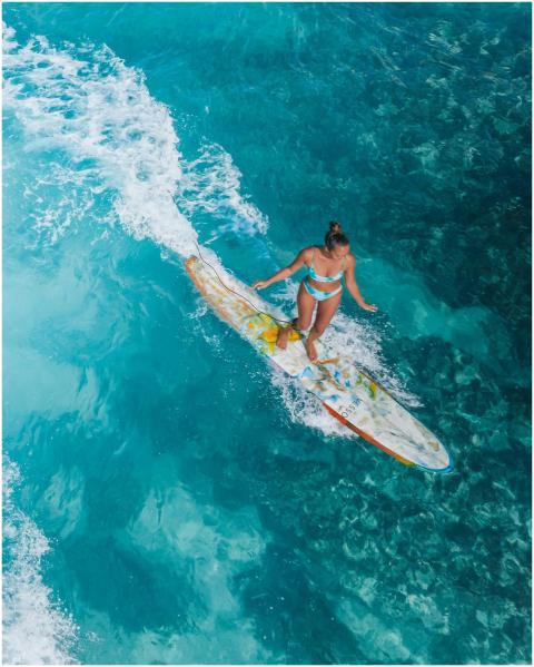 Aerial shot of a woman surfing on vibrant turquois