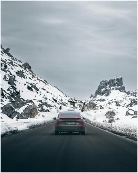 A maroon car driving through a snow-covered mounta