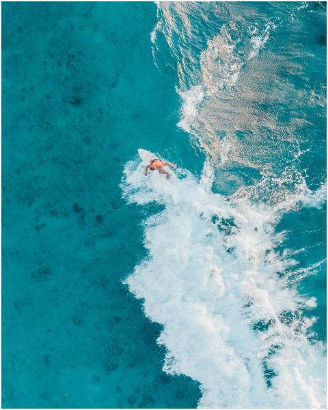 Aerial shot of a surfer riding turquoise waves in