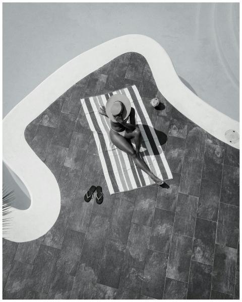 Woman sunbathing by pool, wearing a hat, captured