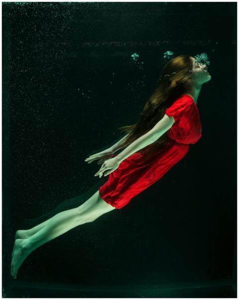 A woman in a red dress gracefully floats underwate