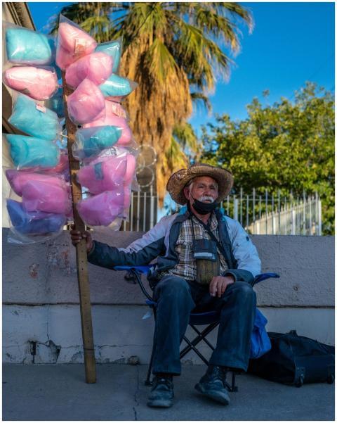 Elderly man sits with colorful cotton candy for sa