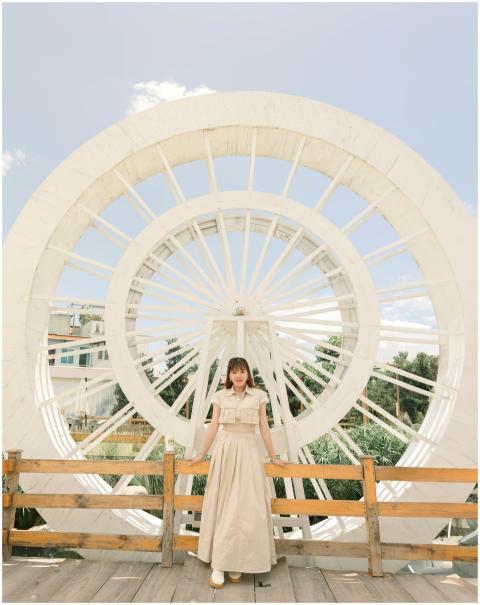 Woman in beige dress stands by a large white wheel