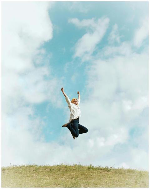 A person jumping energetically on a grassy hill un