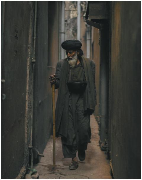 A senior adult with a beard and walking stick stro