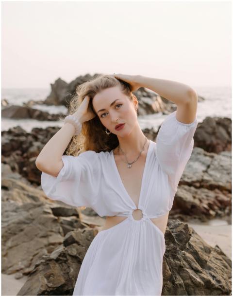 Stylish woman in white dress poses by the ocean on