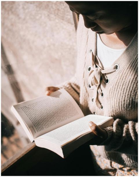 A young woman in a cozy sweater reading a book by