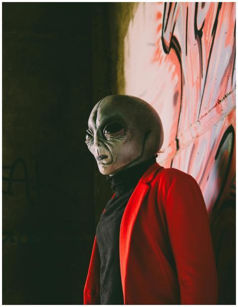 Alien figure wearing a red jacket stands against g