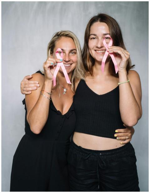 Two women smiling and holding pink ribbons for bre