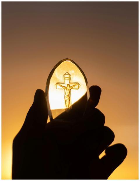 A silhouetted hand holds a crucifix against a vibr