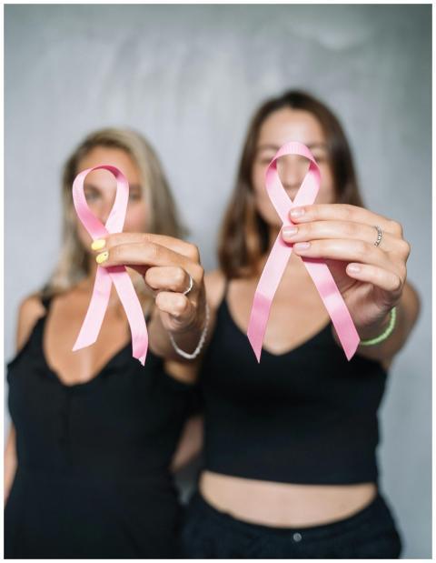 Two women holding pink ribbons, symbolizing breast