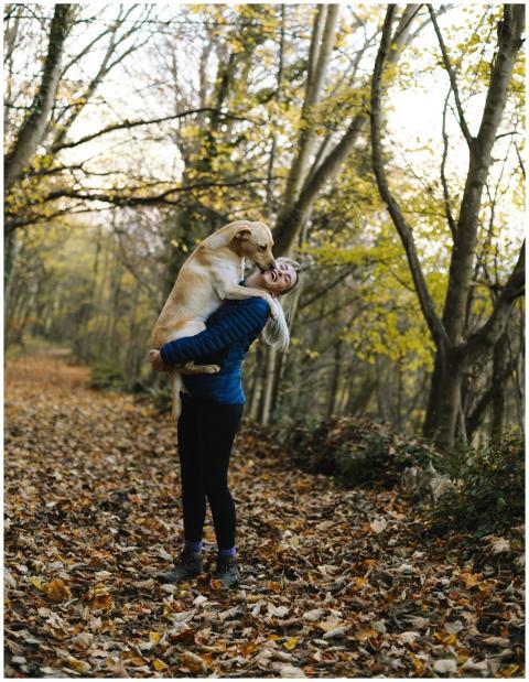 A woman joyfully embraces her dog on a foliage-cov