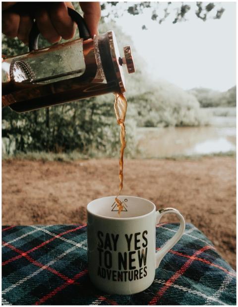 Coffee poured into a mug with adventure-themed tex
