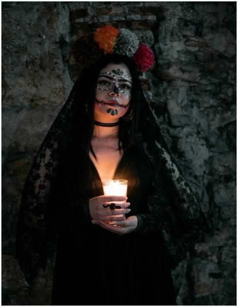 Woman with face paint holding candle in dark, atmo