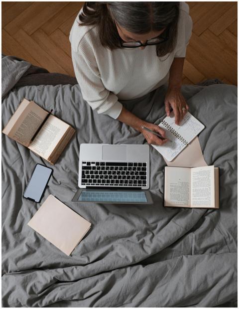 Senior woman taking notes on a bed with a laptop,