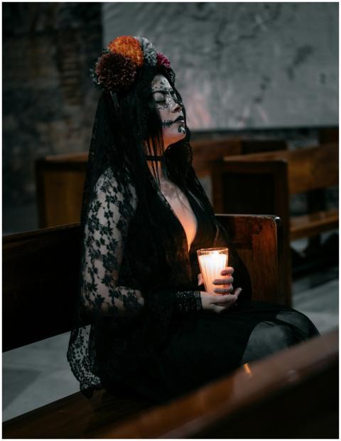 A woman in gothic attire sits with a candle, creat
