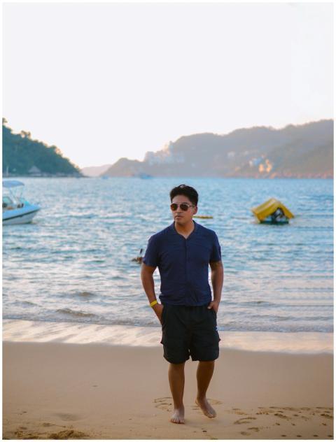 A man walks along a calm beach at sunset, with boa