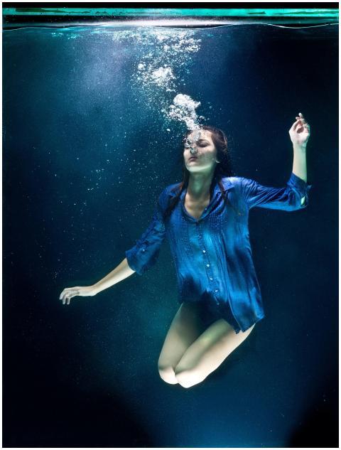 A woman in blue shirt poses elegantly underwater w