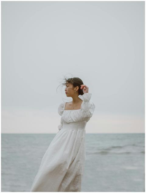A thoughtful young woman in a white dress stands b