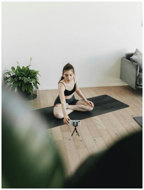 Woman in yoga pose on mat, filming herself with a