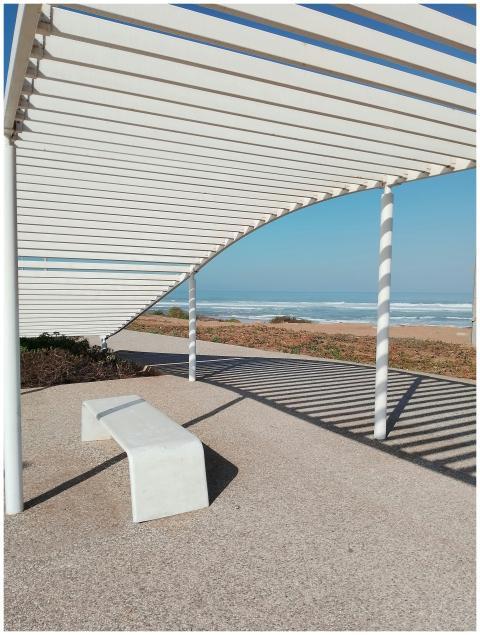 A modern pergola casting shadows by a beach in Cas