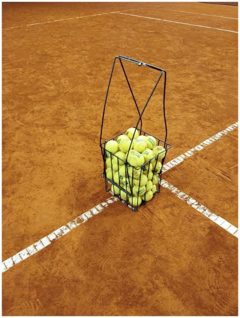A basket filled with tennis balls placed on a clay