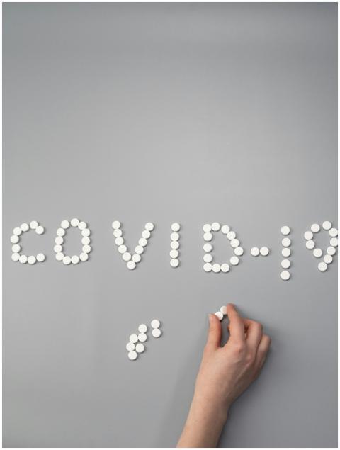 White pills spelling 'COVID-19' on gray surface wi