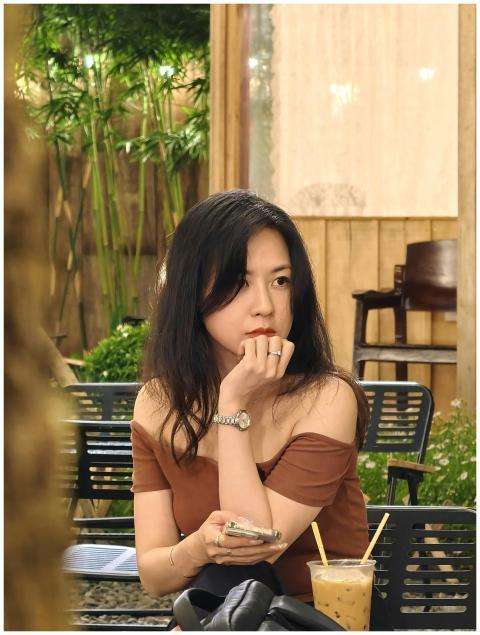 Asian woman with drink in cozy café, deep in thoug