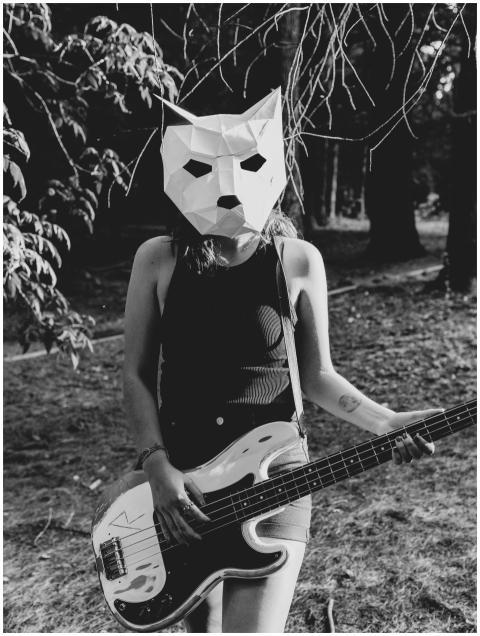 Woman with mask playing electric guitar outdoors,