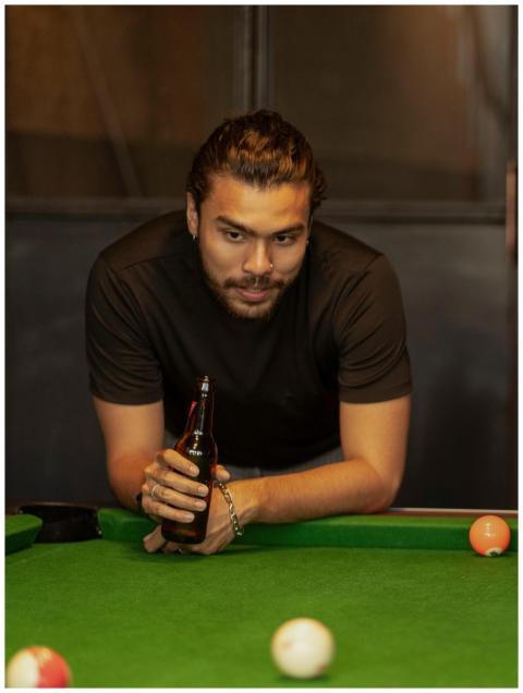 Man holding a beer bottle by a snooker table, read