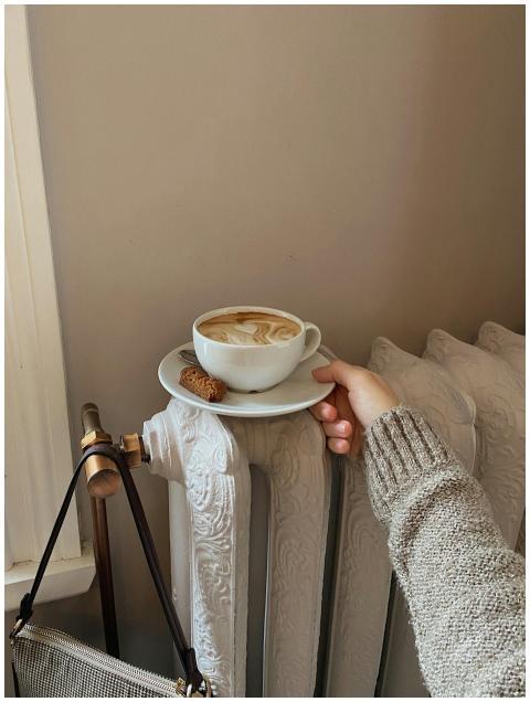 A hand holds a coffee cup atop a vintage heater, c