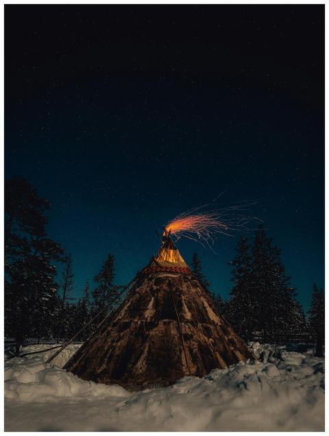 A glowing tent with fire under a starry winter sky