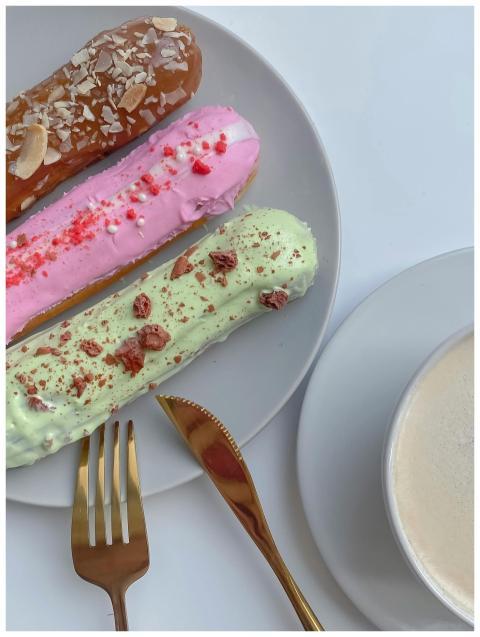 Three vibrant eclairs with toppings alongside a cr