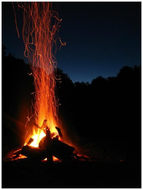 A vibrant campfire with sparks rising against a se