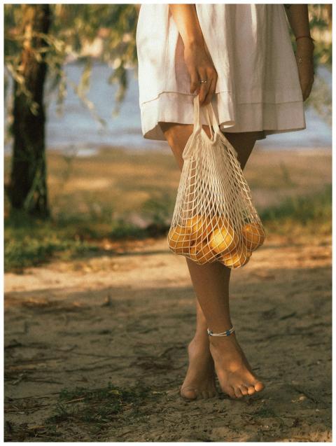 Woman in white dress holding a mesh bag of lemons,
