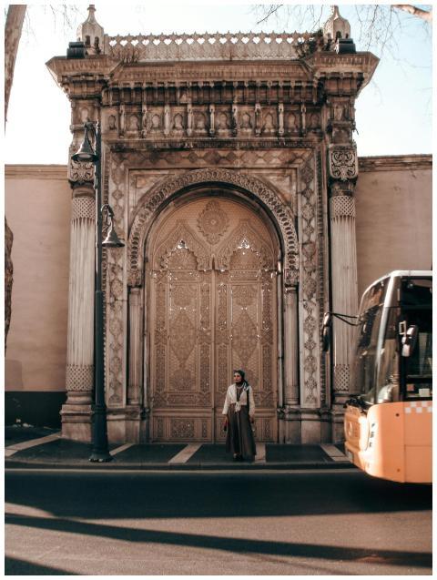 A person stands by a majestic ornate gate with a b
