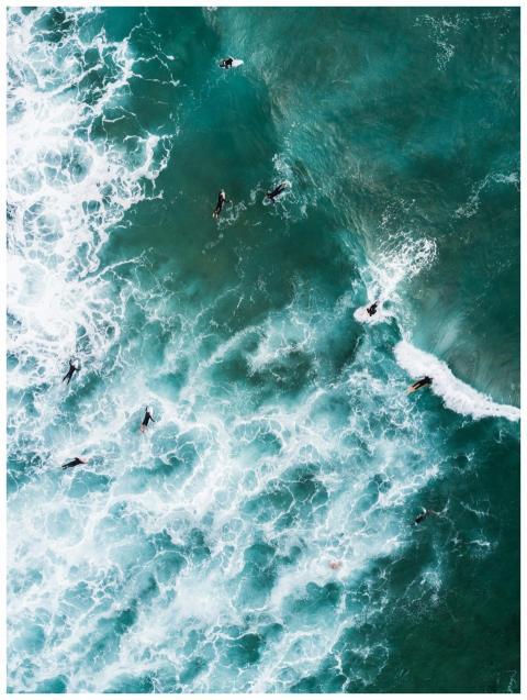 Aerial shot of surfers catching ocean waves with v