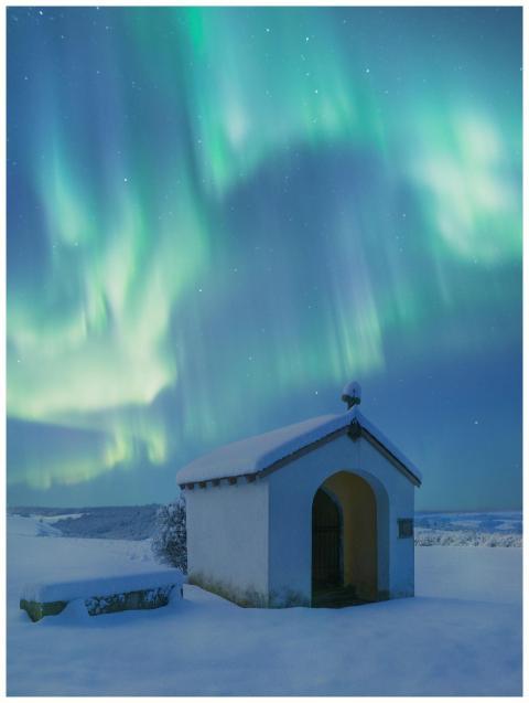 A snowy chapel stands beneath vivid green auroras
