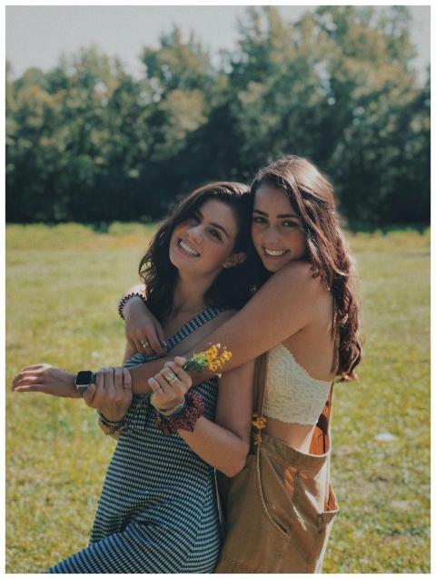 Two smiling sisters embracing in a sunlit park, en