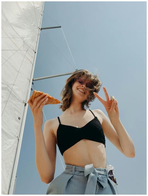 Smiling woman on a yacht under a sail, holding piz