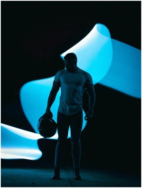 A muscular man stands holding a helmet with striki