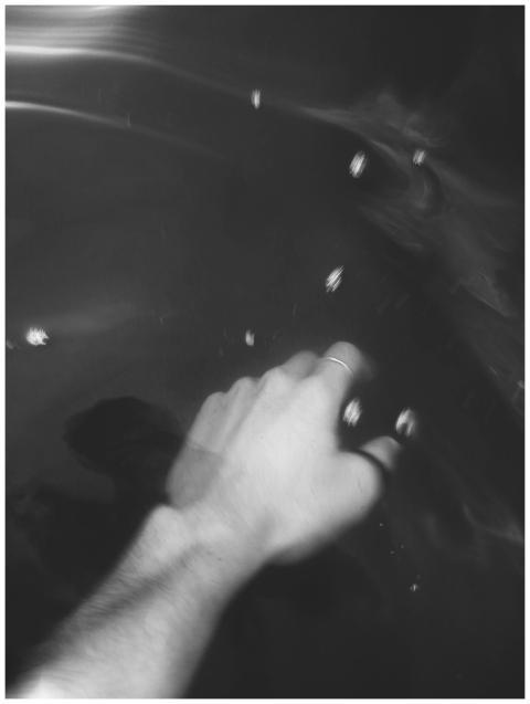 A hand reaches into dark, splashing water in this
