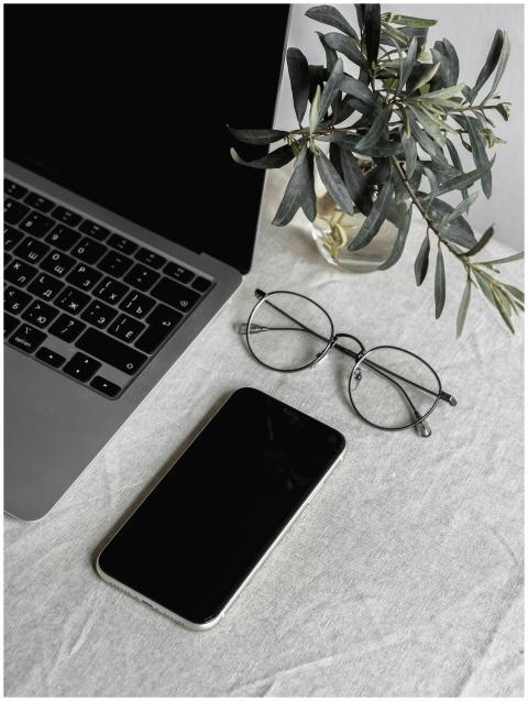 Flat lay of a laptop, smartphone, glasses, and pla