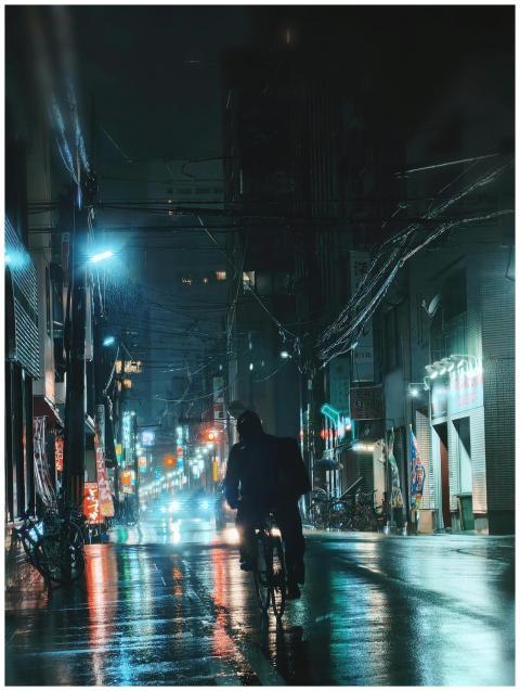 A man cycling through the rainy, illuminated stree