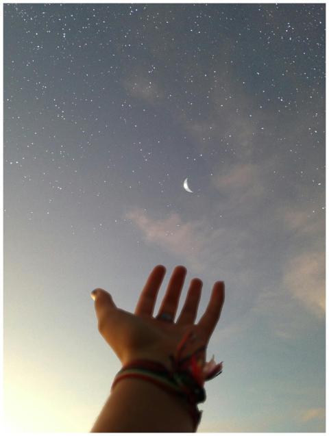 A hand reaches towards a crescent moon against a b